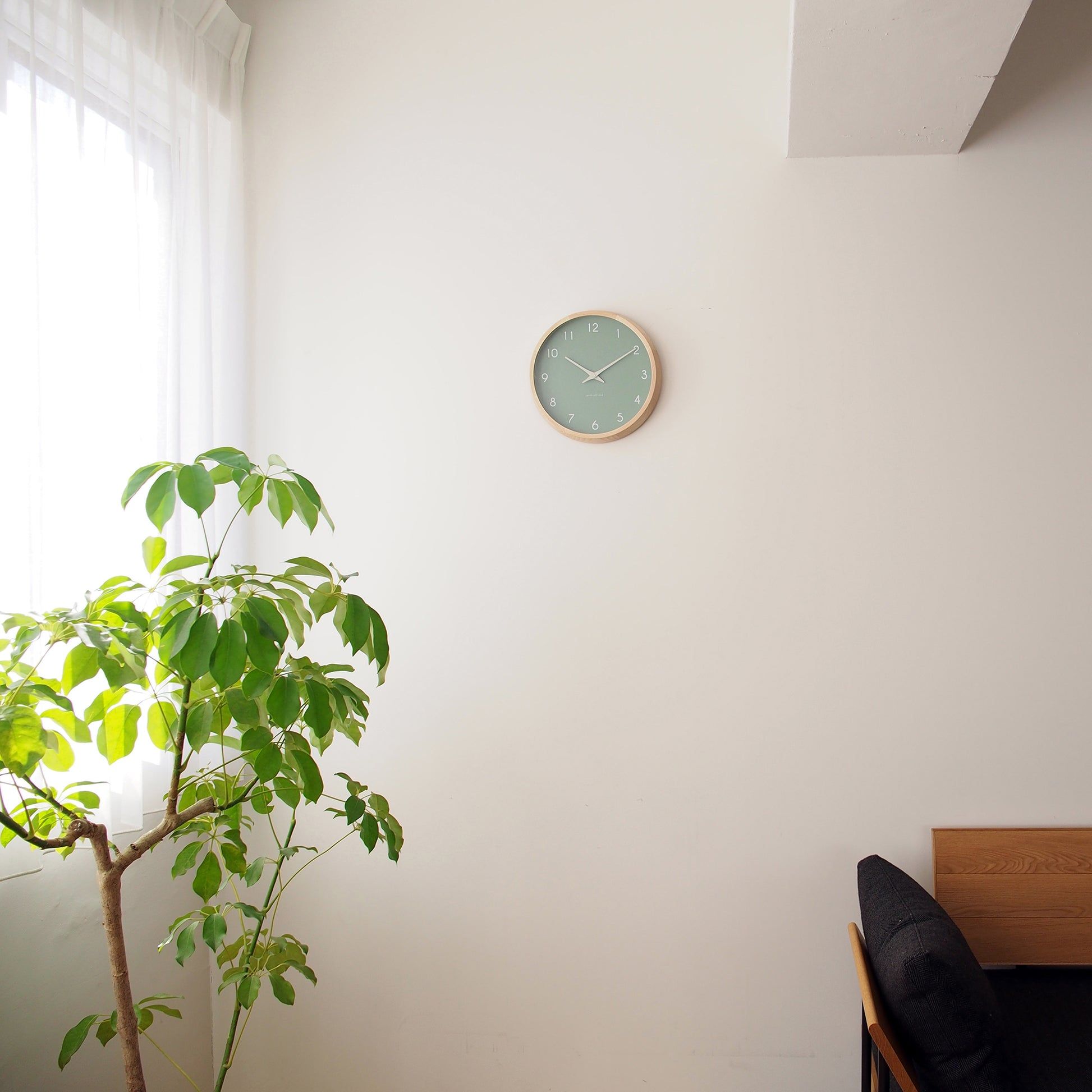 Kleine Wanduhr an der Wand mit grünem Zifferblatt und Holzrand