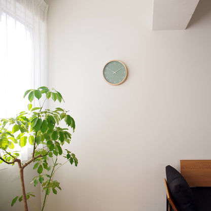 Kleine Wanduhr an der Wand mit grünem Zifferblatt und Holzrand