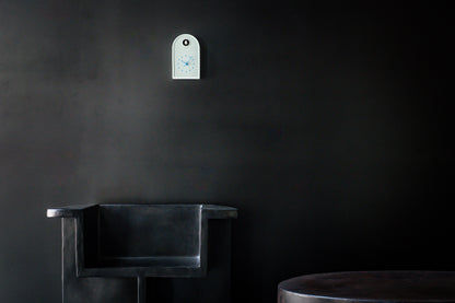 Kleine mintblaue Wanduhr mit Lochmuster an dunkler Wand