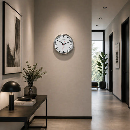 Runde Wanduhr an der Wand: silberner Rand, weißes Zifferblatt, schwarze Markierungen, rote Zeiger