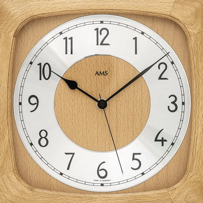 Nahaufnahme der Holz-Wanduhr: rundes Holz-Zifferblatt, schwarze Zeiger, AMS-Logo im Zentrum