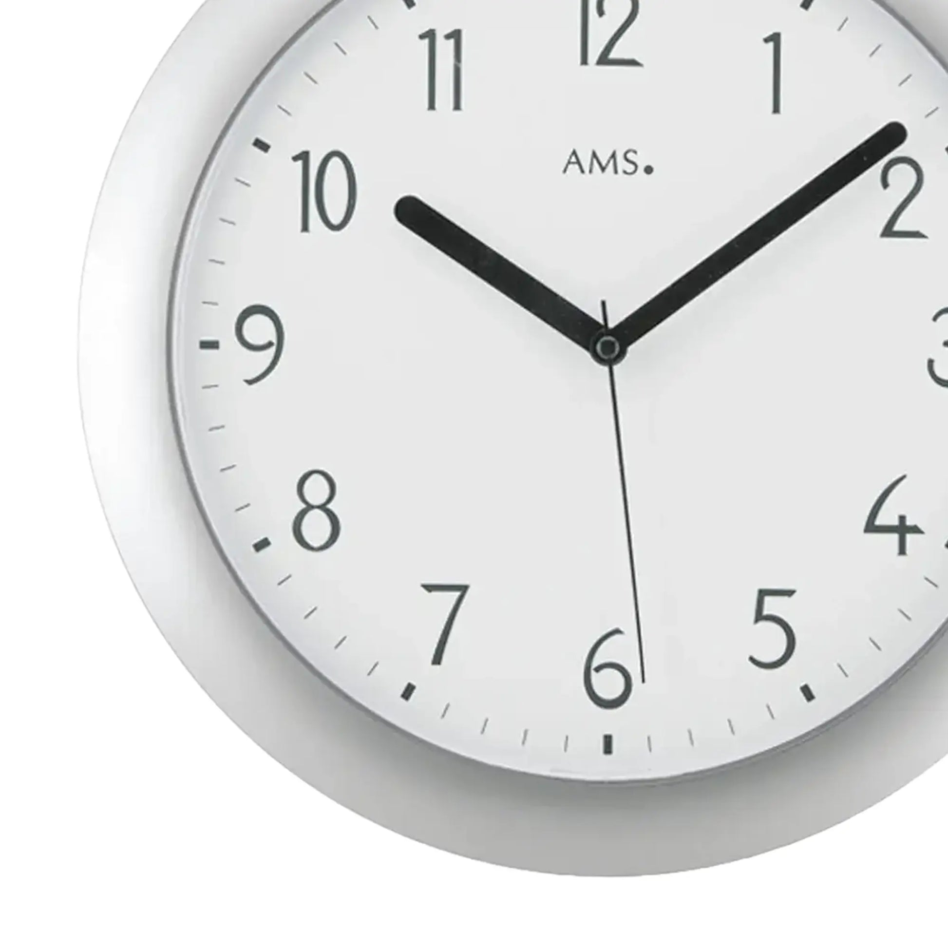 Nahaufnahme Funk-Wanduhr: silbernes Gehäuse, weißes Zifferblatt, schwarze Zeiger, AMS-Logo.