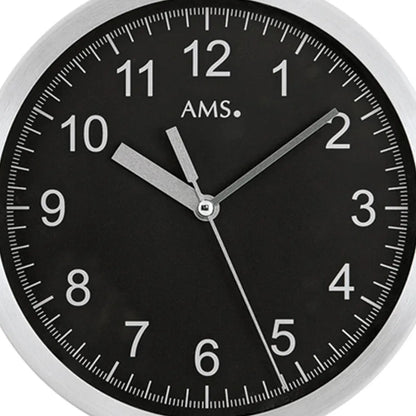 Nahaufnahme Wanduhr mit schwarzem Ziffernblatt, AMS-Schriftzug und Aluminiumrahmen