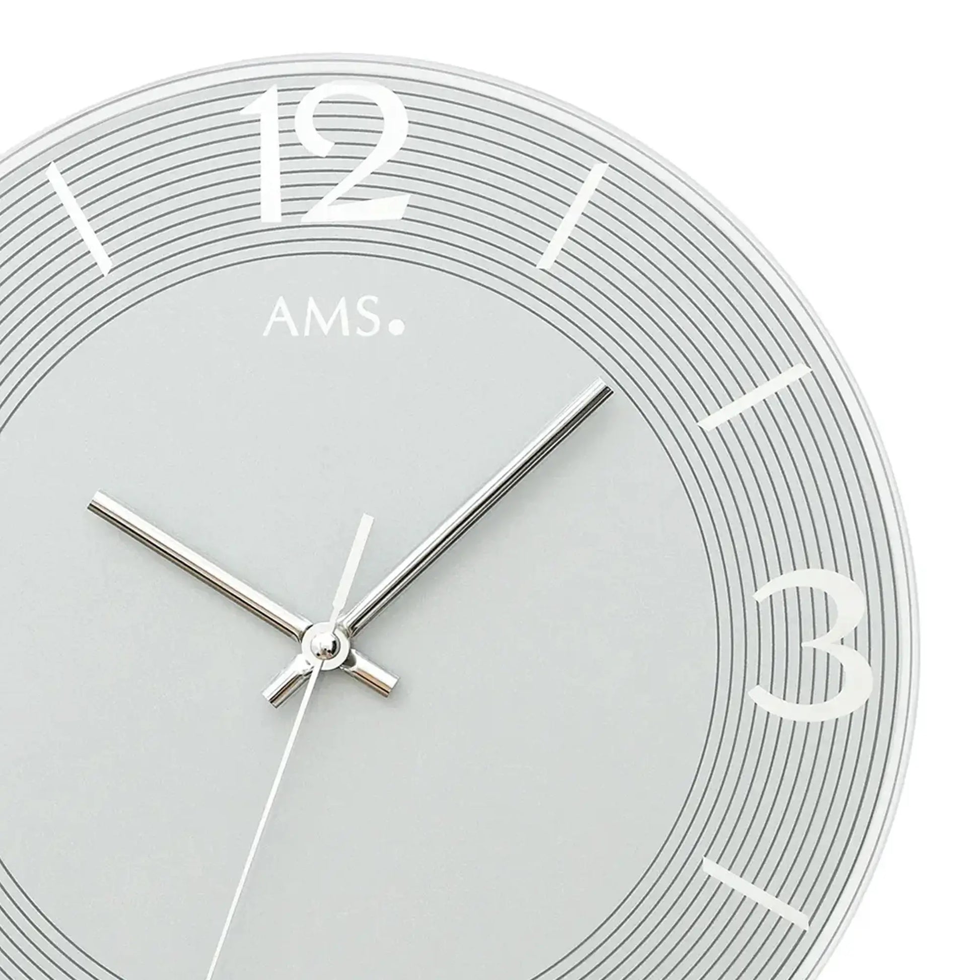 Nahaufnahme der blaugrauen AMS-Wanduhr: römische Ziffern, schmale Zeiger, feine Zeitmarken.