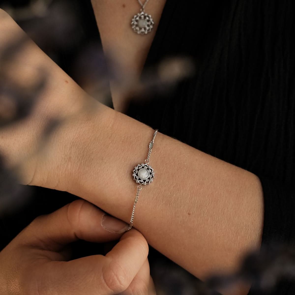 Silbernes Armband mit rundem grauem Stein im Blütenornament am Handgelenk.
