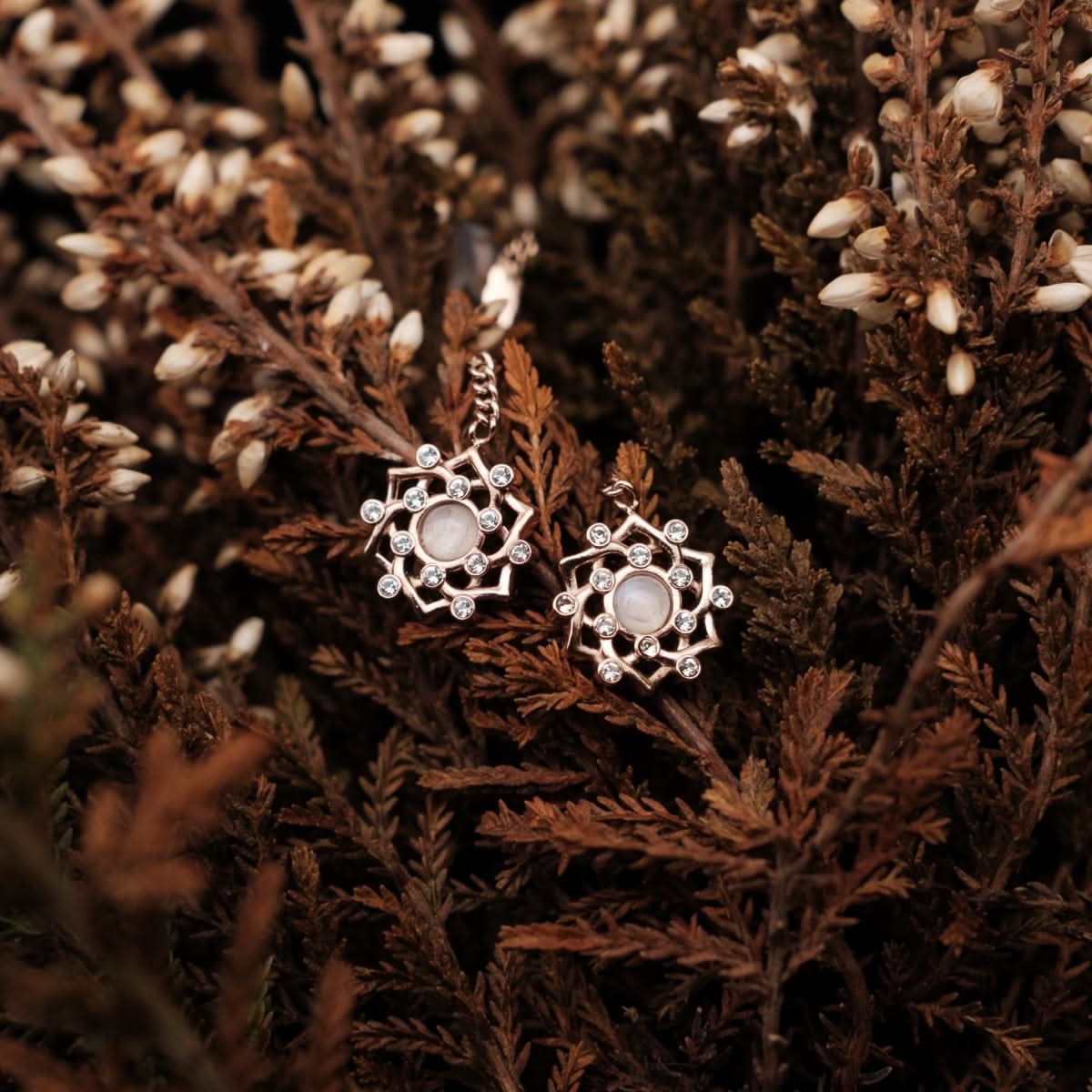 Ohrringe im Dekor: runder Stein im floralen Kranz mit schimmernden Ziersteinen und Kettenzug