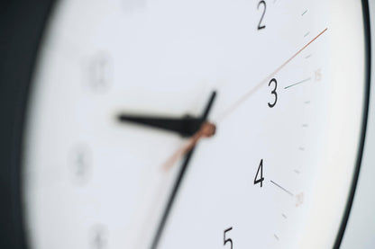 Nahaufnahme der Uhrzeiger auf dem weißen Zifferblatt der Wanduhr mit schwarzem Rand.