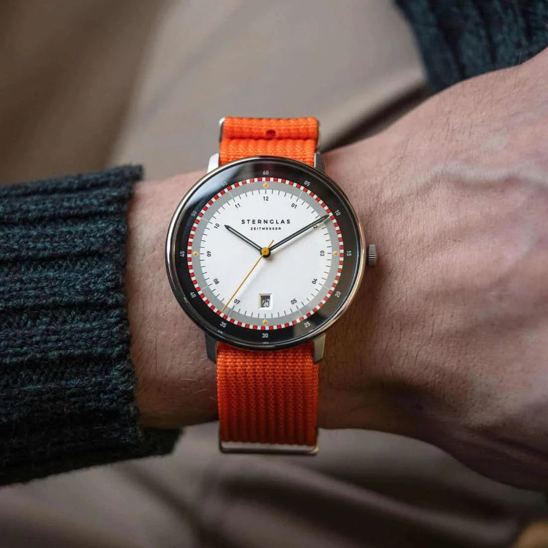 Herrenuhr am Handgelenk mit orangefarbenem Textilarmband, rundes weißes Zifferblatt