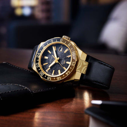 Armbanduhr auf Unterlage: schwarzes Lederband, goldfarbenes Gehäuse, dunkles Zifferblatt.