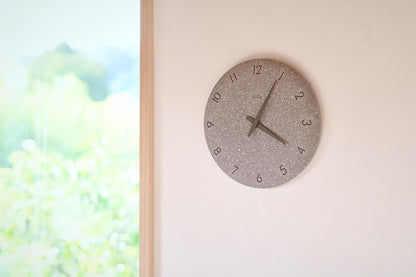 Kleine graue Wanduhr mit gesprenkeltem Stein-Look an heller Wand, Zeiger sichtbar