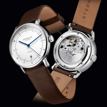 Herrenuhr in zwei Ansichten übereinander: weißes Zifferblatt mit blauen Zeigern und Uhrwerk im Gehäuse