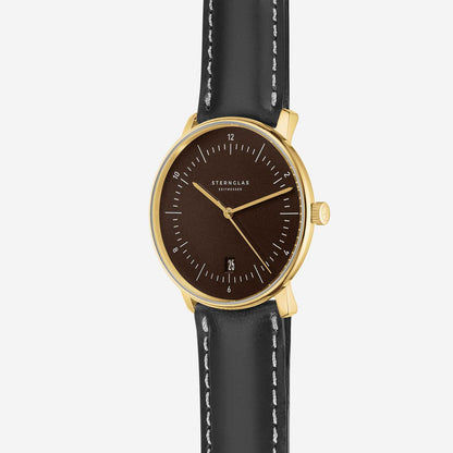 Sternglas Herrenuhr mit schwarzem Lederband, rundem braunem Zifferblatt und goldfarbenen Indexen