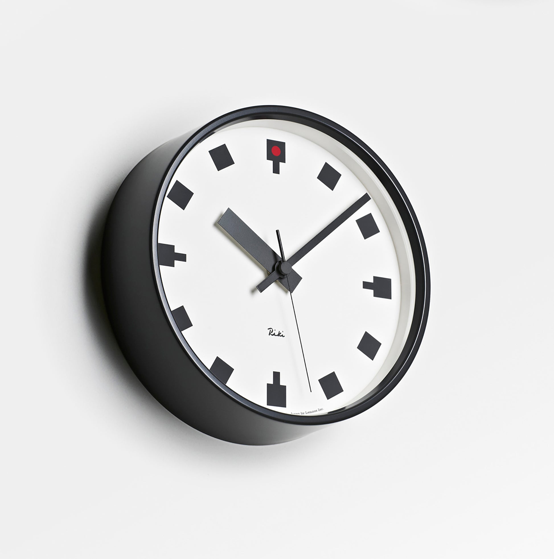 Rundliche Wanduhr mit weißem Zifferblatt, schwarzem Gehäuse und roten Details am Zifferblatt