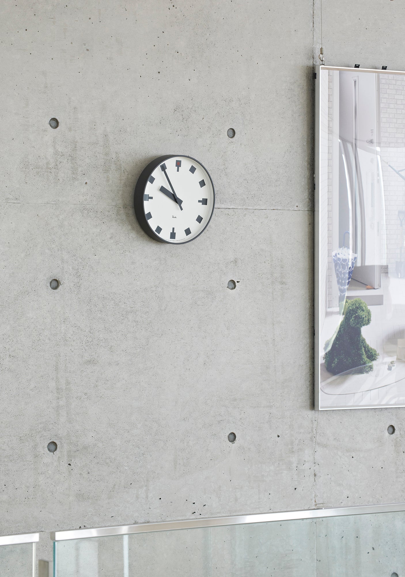 Kompakte Wanduhr mit weißem Zifferblatt, schwarzen Zeigern und roten Akzenten, an Betonwand