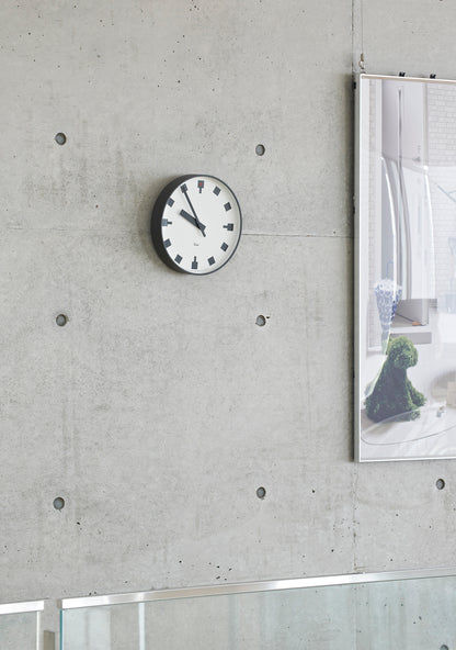 Kompakte Wanduhr mit weißem Zifferblatt, schwarzen Zeigern und roten Akzenten, an Betonwand