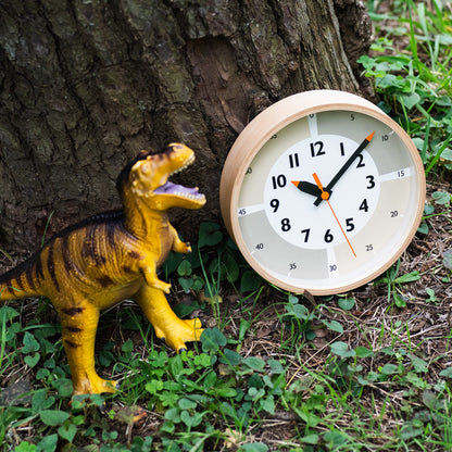 Beige Wanduhr mit arabischen Zahlen und Zeigern, auf Gras neben Dinosaurierfigur.