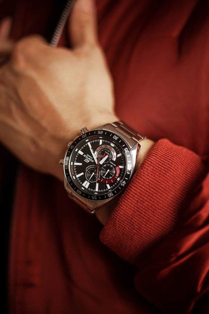 Herren-Chronograph mit schwarzem Zifferblatt und roten Details, getragen mit roten Strickbündchen.