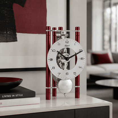 Skelett-Tischuhr mit weißem Ziffernblatt, schwarzem Minutenzeiger und roten Metallstreben