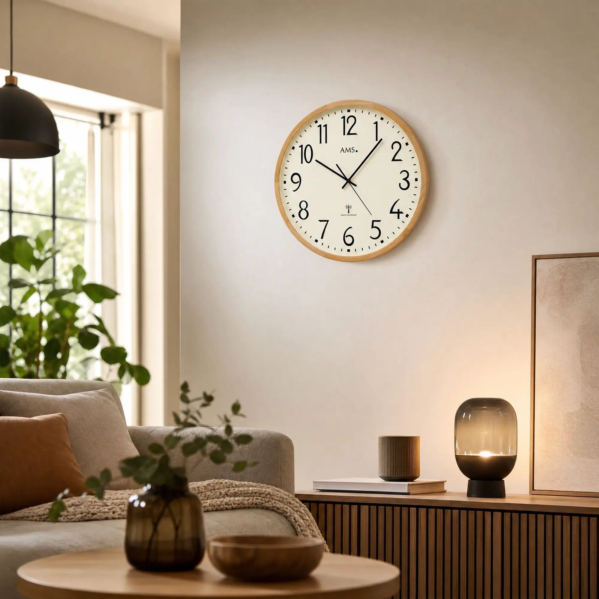 Wanduhr an der Wand über Wohnmöbeln, beiges Ziffernblatt mit schwarzen Zeigern im Holzrahmen.