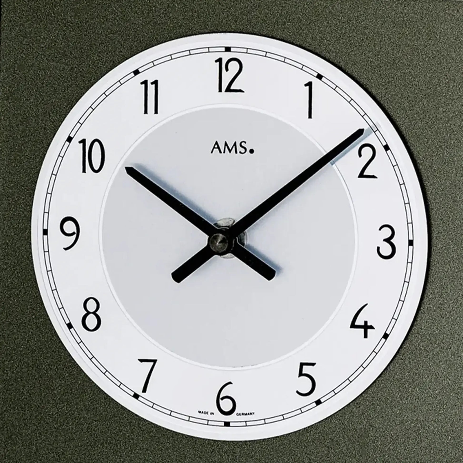 Anthrazitfarbene Tischuhr mit weißem Zifferblatt, schwarzen Zeigern und AMS-Logo (Detail).