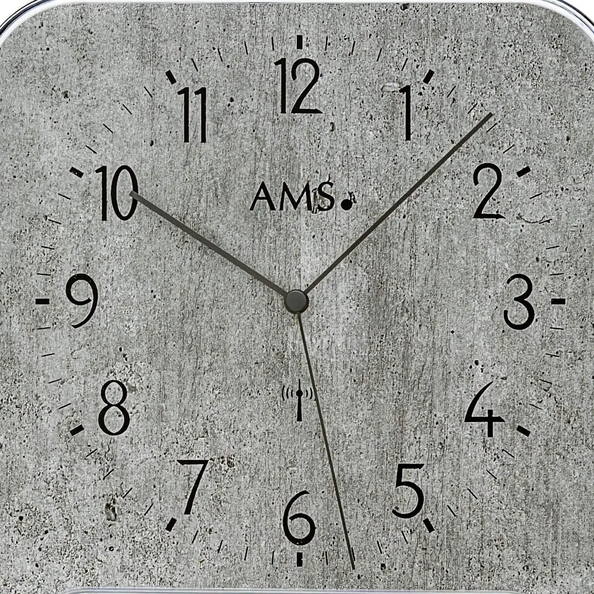 Wanduhr-Zifferblatt mit AMS-Schriftzug, Analogzeiger auf grauem Beton-Look mit Skala