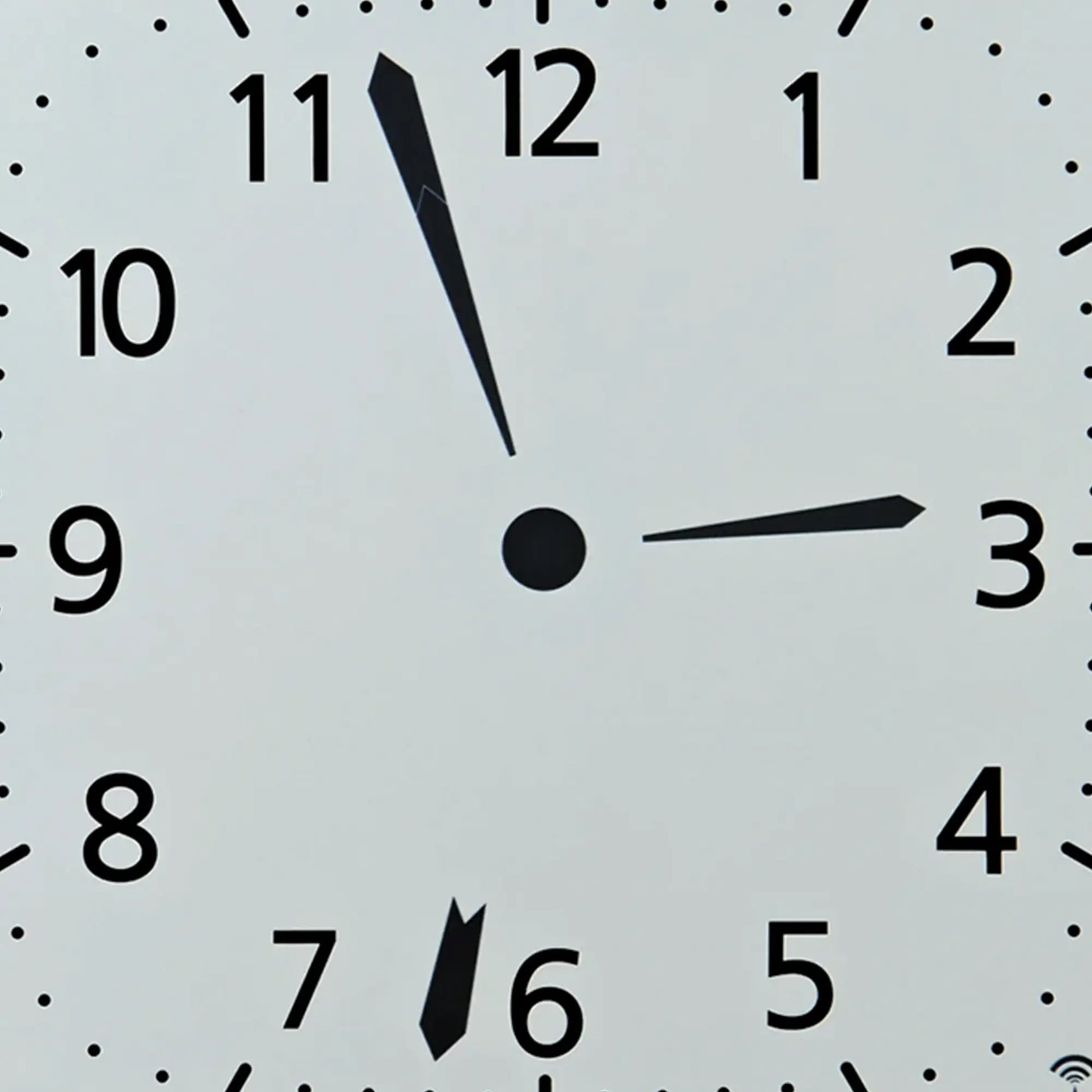 Nahaufnahme der weißen Funk-Wanduhr: schwarze Zeiger, Punkte als Minutenmarken, Ziffern 1–12.