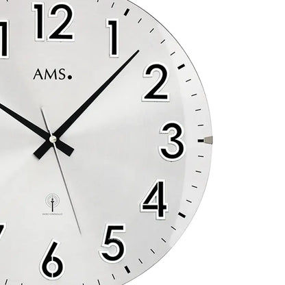 Detail der silbernen Wanduhr: weißes Zifferblatt, schwarze Zeiger, Zahlen 1–6, AMS