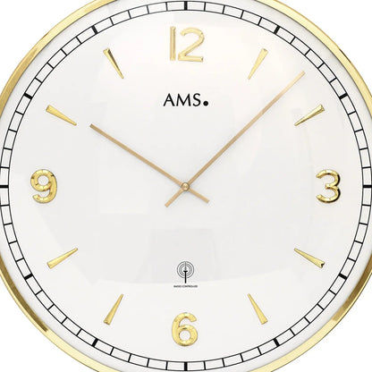 Nahansicht der Wanduhr: weißes Ziffernblatt, goldene Stundenmarken, AMS-Logo