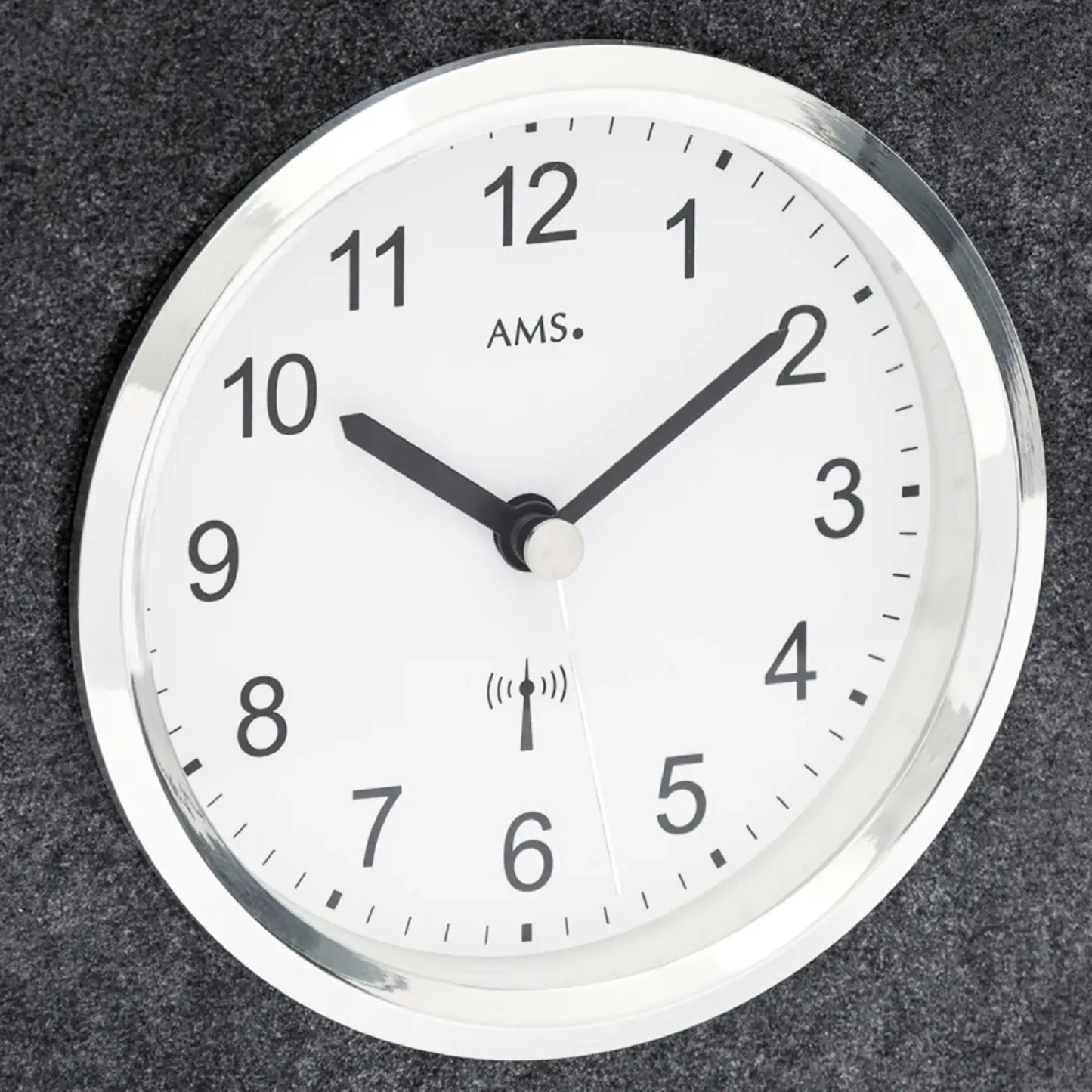 Nahaufnahme: rundes Zifferblatt mit AMS-Schrift und Funkwellen-Symbol, schwarze Zeiger.