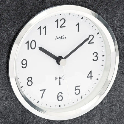 Nahaufnahme: rundes Zifferblatt mit AMS-Schrift und Funkwellen-Symbol, schwarze Zeiger.
