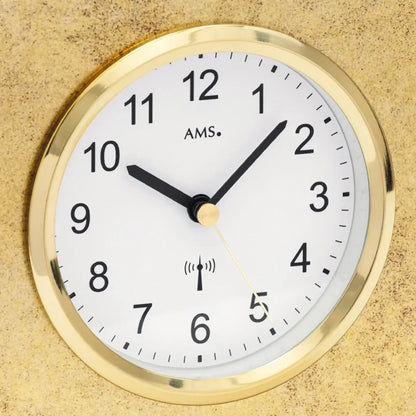 Nahaufnahme Tischuhr: weißes Ziffernblatt mit AMS-Logo, goldener Rahmen, Funk-Symbol