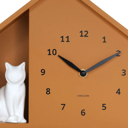Detail der Katzenhaus-Wanduhr: ockerfarbenes Zifferblatt mit Zeigern und weißer Figur